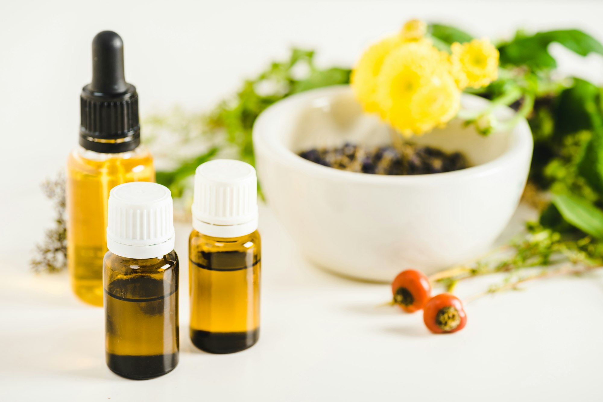 bottles of essential oils and herbs on white surface